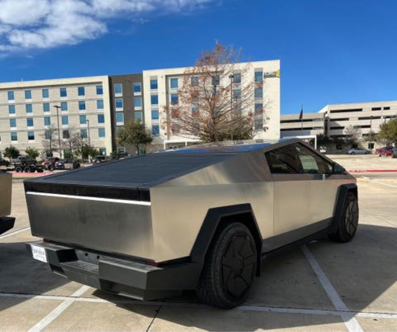 Cybertruck before the wrap, in the original factory stainless steel finish, rear three-quarter view in a parking lot