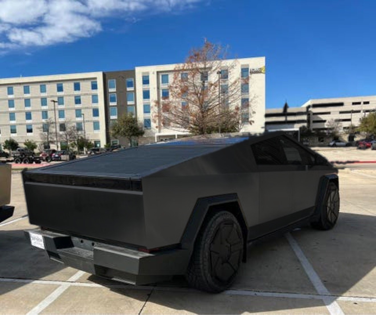 The same Cybertruck photo after the wrap, in matte black — same car, same rear three-quarter view in the same parking lot, only the color changed