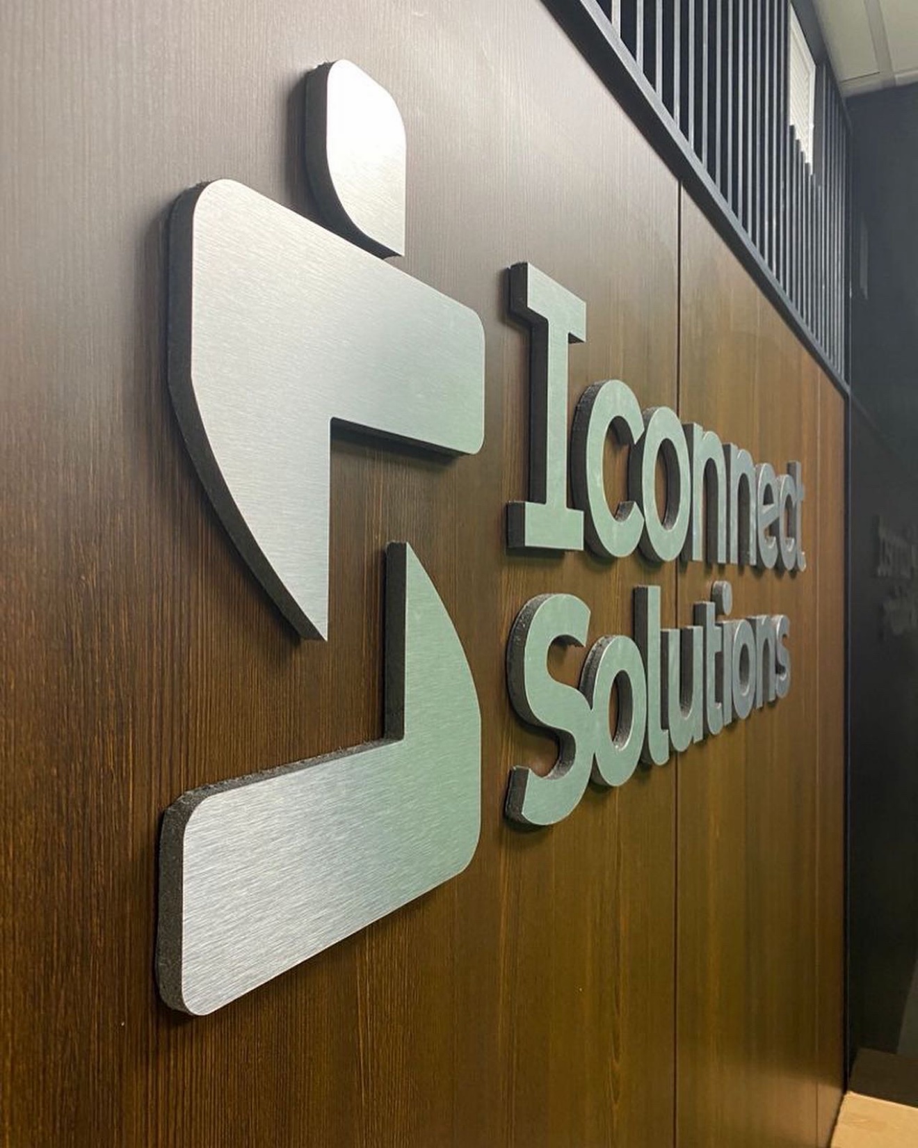 Brushed-metal dimensional letters spelling I Connect Solutions mounted on a wood panel wall