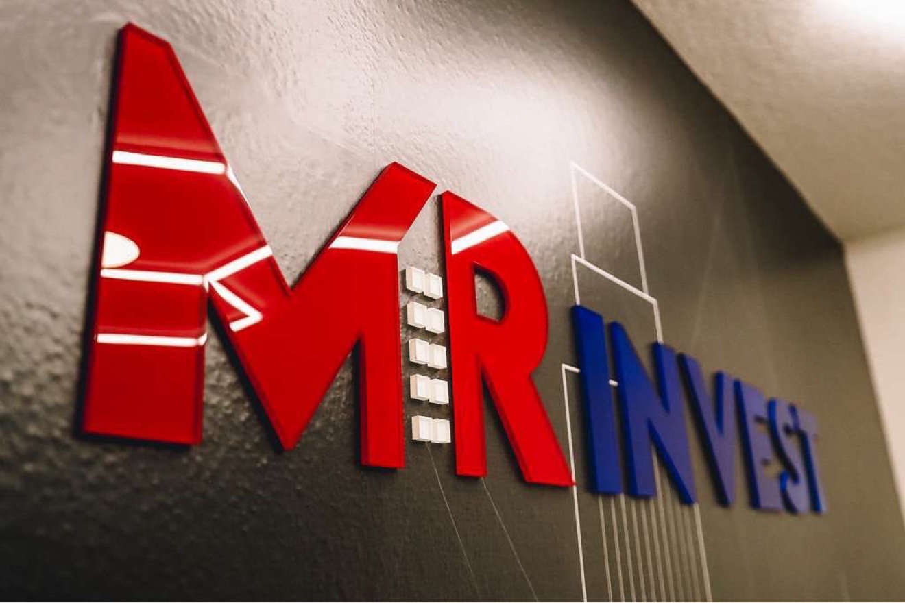 Close-up of glossy red and blue acrylic letters spelling MR Invest on a dark wall