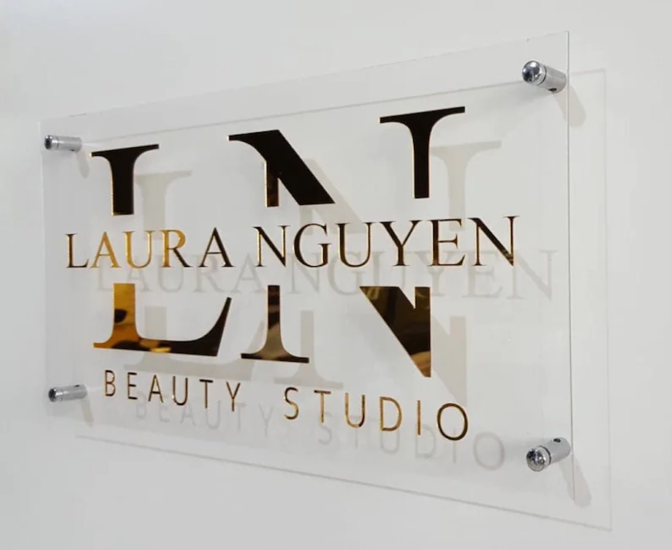 Laura Nguyen Beauty Studio sign in gold and black on a clear acrylic panel with standoffs