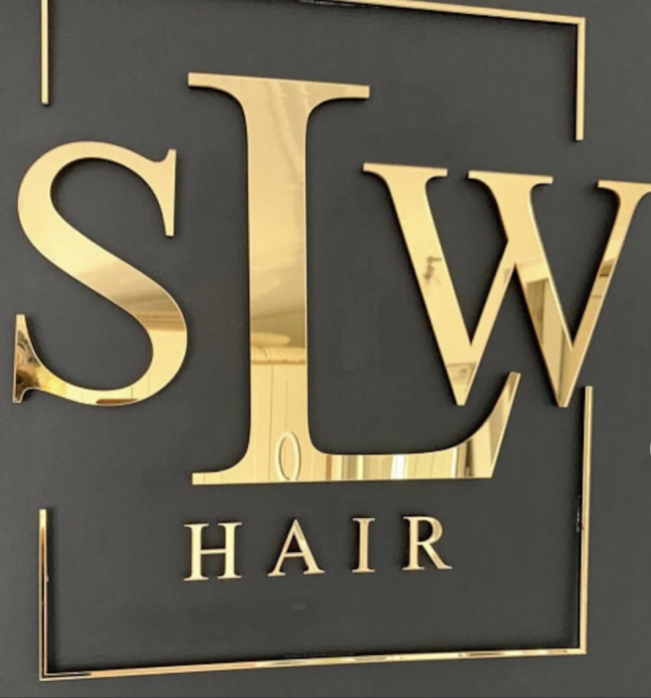 Gold mirror acrylic letters spelling SLW Hair on a black wall