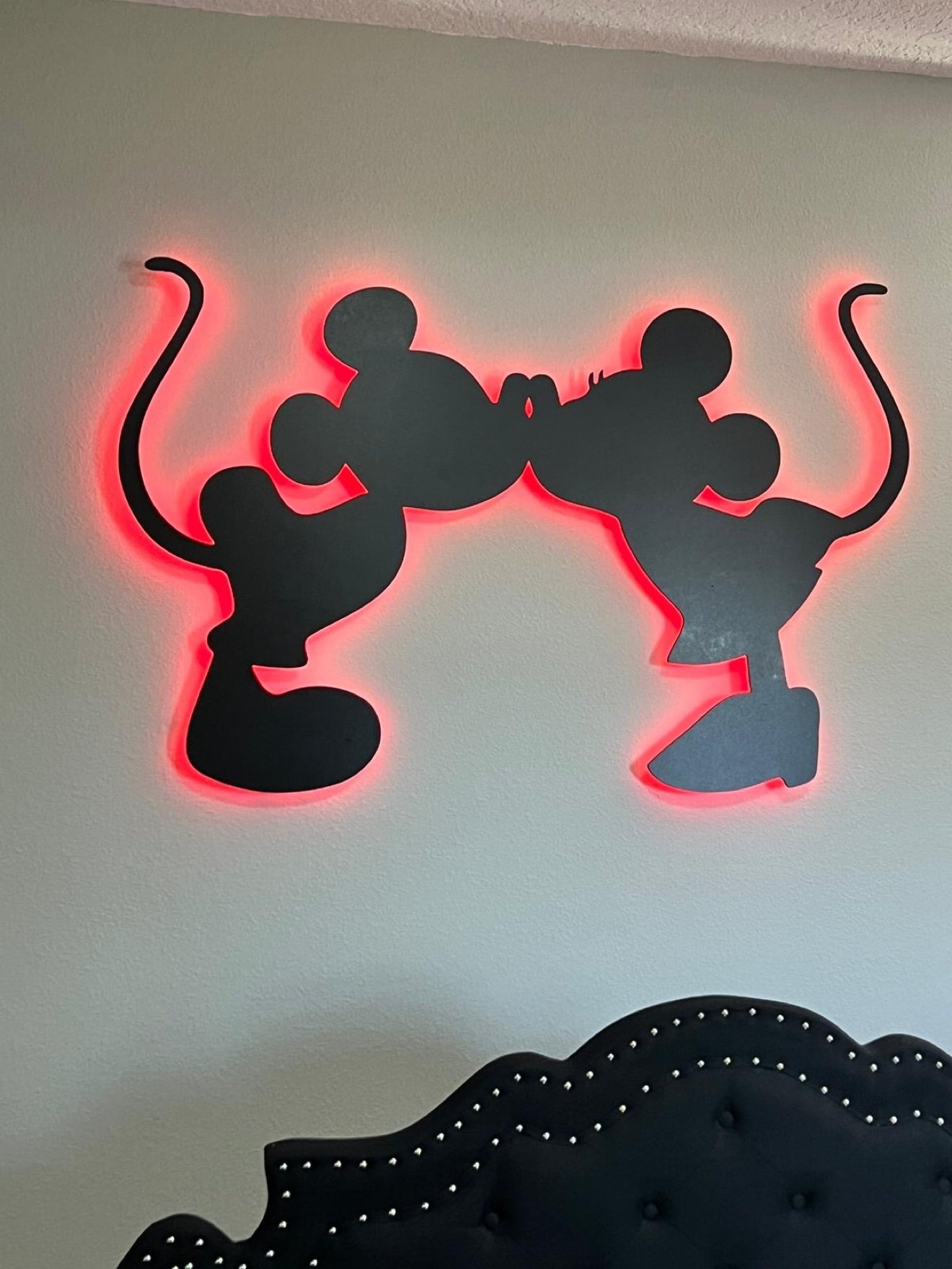 Mickey and Minnie kissing silhouette cutout with a red LED halo above a bed