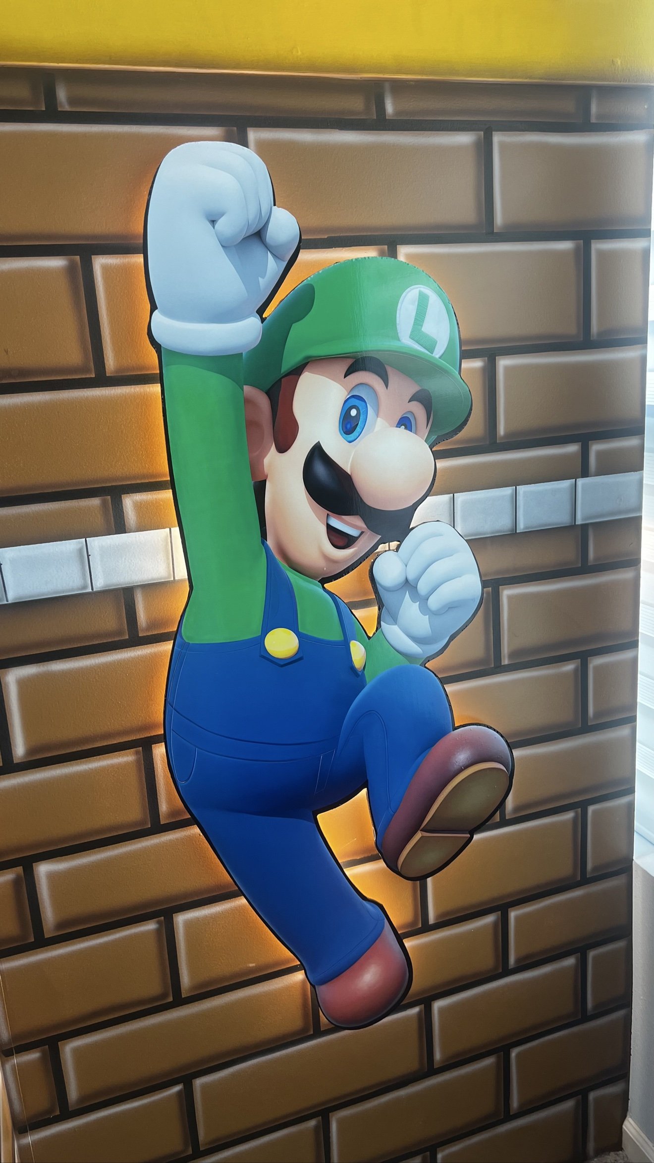 Luigi jumping 3D cutout with a warm LED halo on a brick mural wall