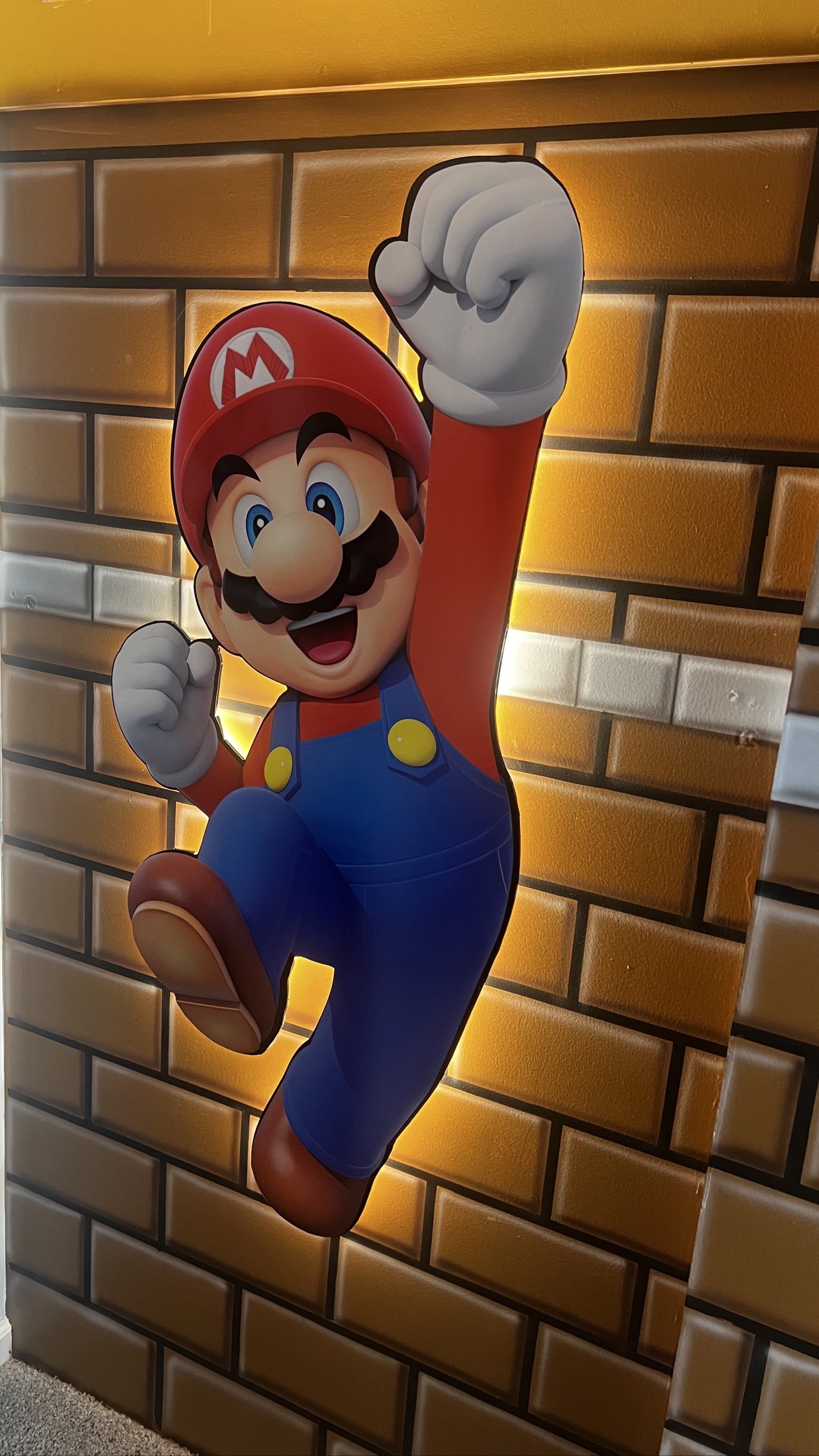 Mario jumping 3D cutout with a warm LED halo on a brick mural wall